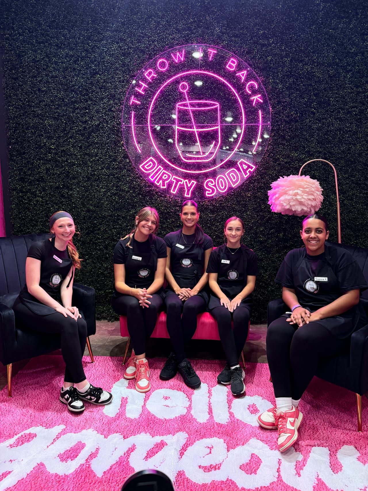 The crew in front of the neon Throw It Back Dirty Soda logo wall